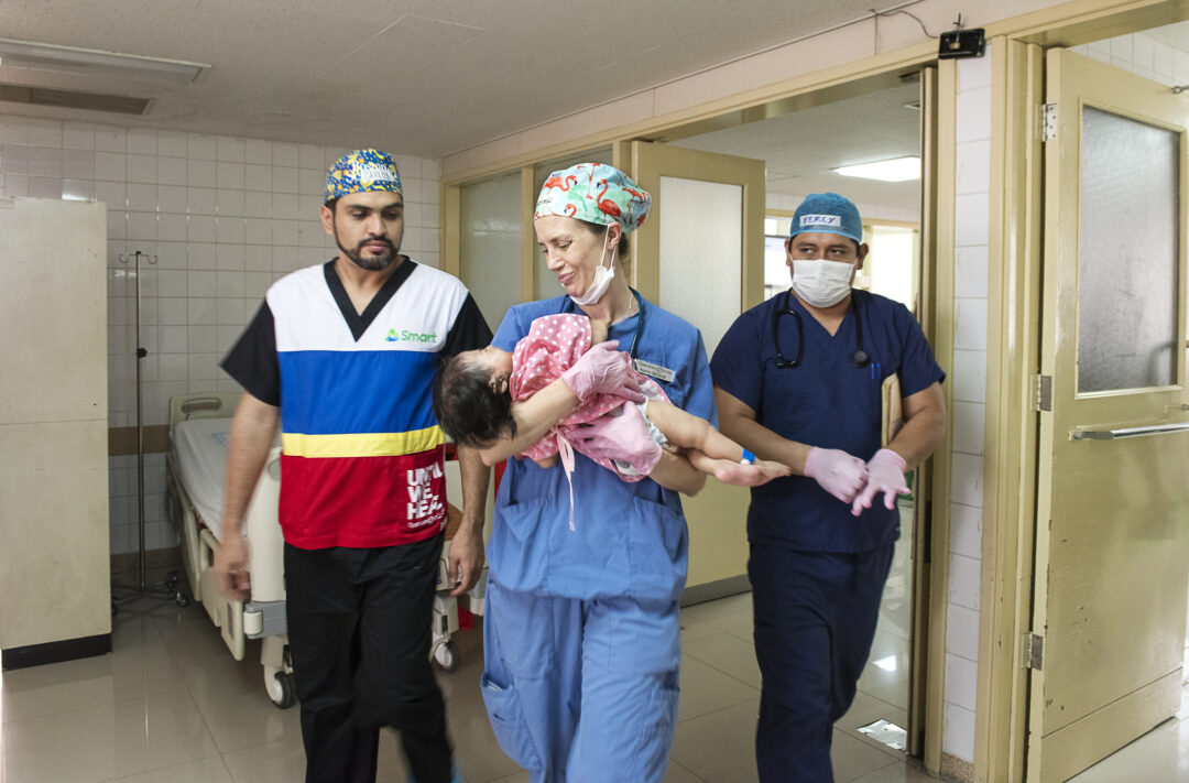 Bolivian Volunteer cleft surgeon Dr. Carlos Hugo Dorado, left, and paediatric anaesthesiologist Dr. Karin Strand, centre, carry Heydi out of the operating room toward the waiting arms of her grandmother, Claudina. Photo: Margherita Mirabella